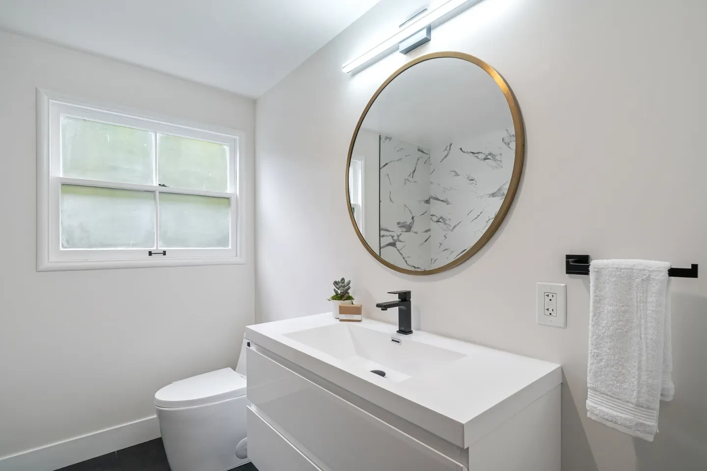 Modern bathroom with white vanity, gold round mirror and black fixtures